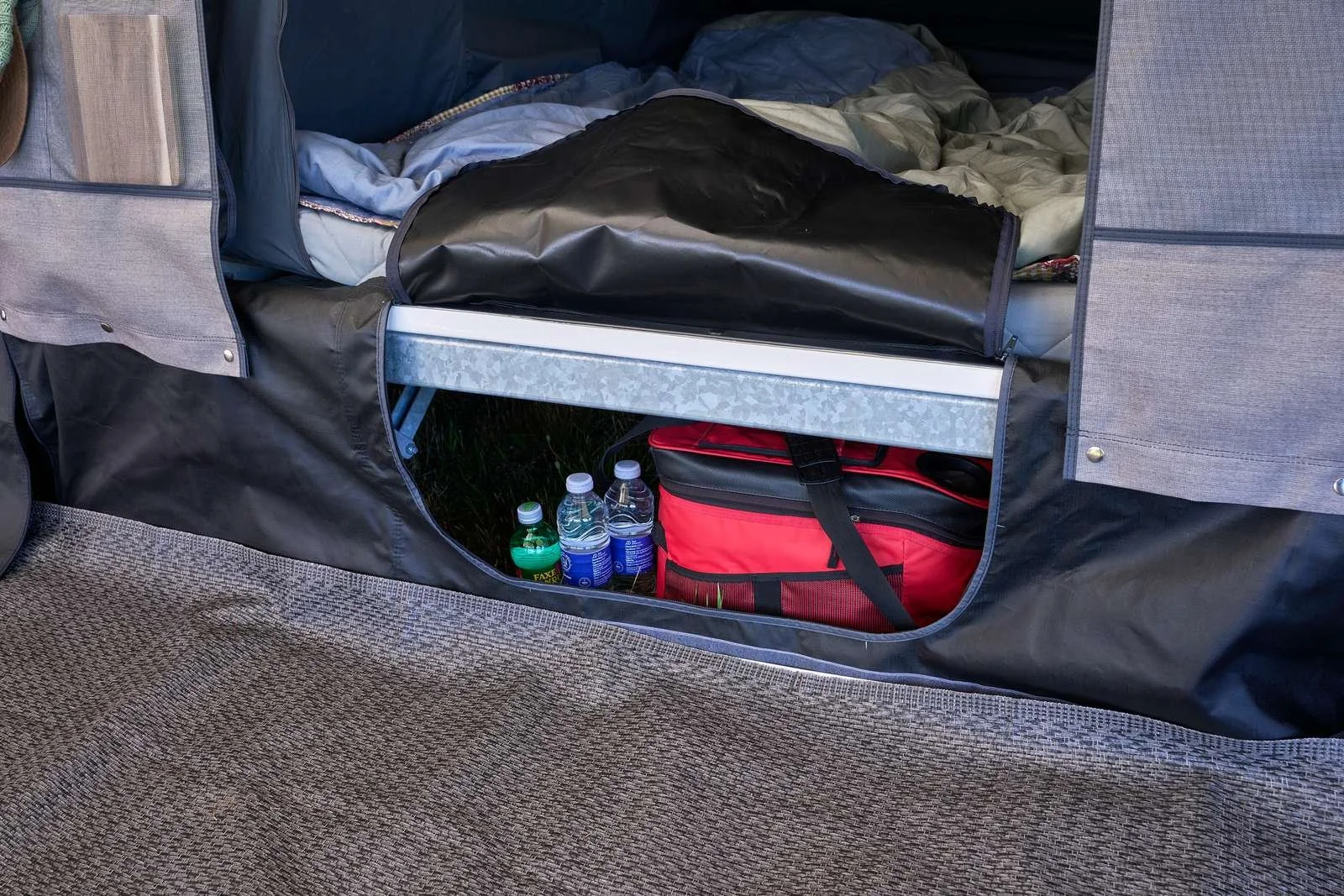 Under a bed with an opening showing bottles of water and a red bag stored underneath.