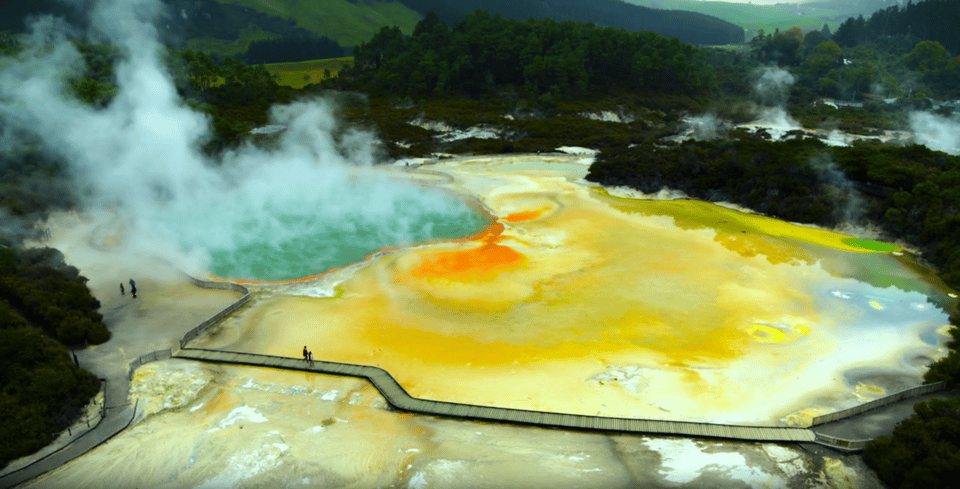 A geothermal hot spring with colorful mineral deposits and steaming water, surrounded by lush green hills.
