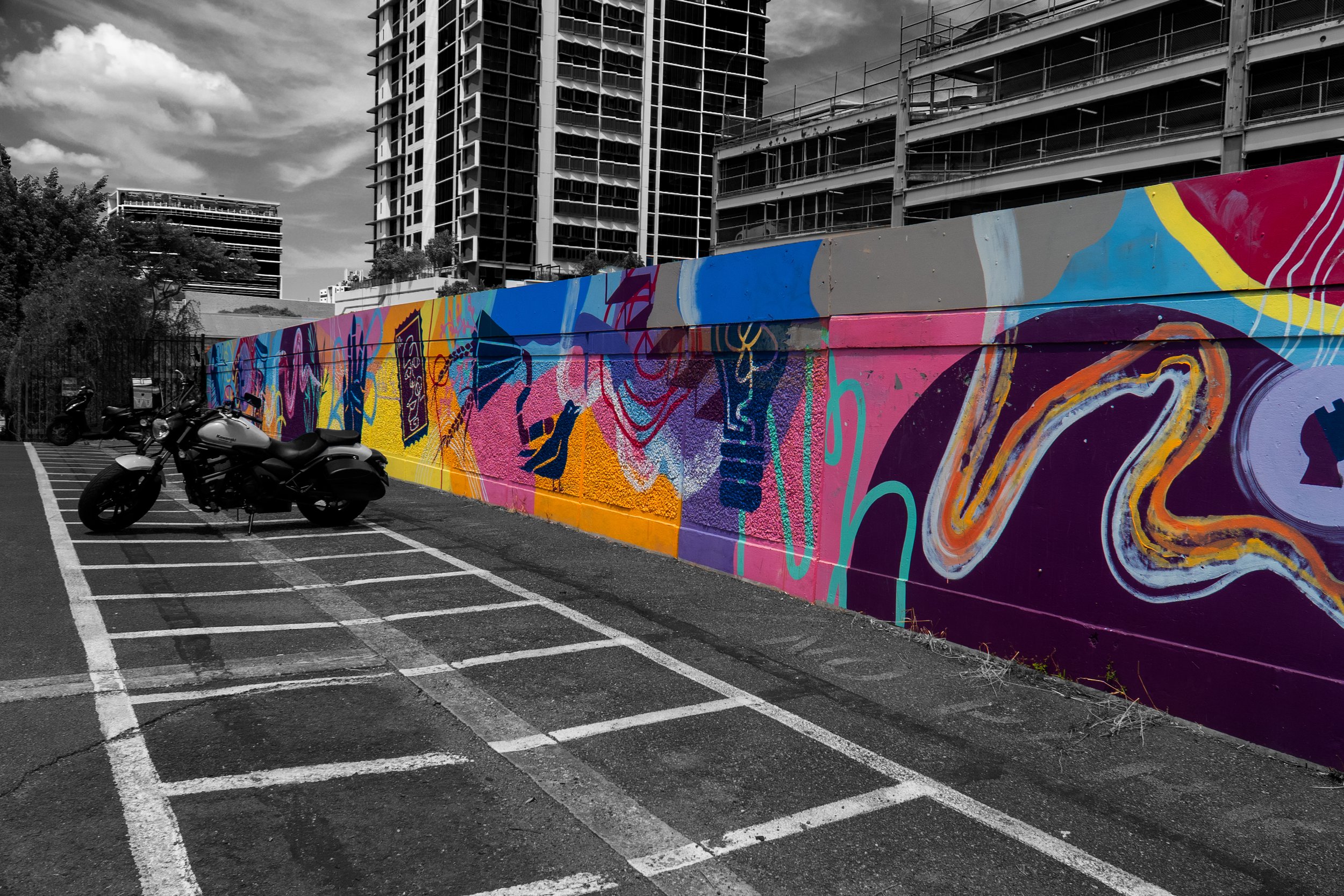 This photograph captures a colourful mural stretching along an urban wall. The vibrant patterns contrast with the surrounding architecture and pavement, celebrating the role of public art in transforming everyday city spaces.