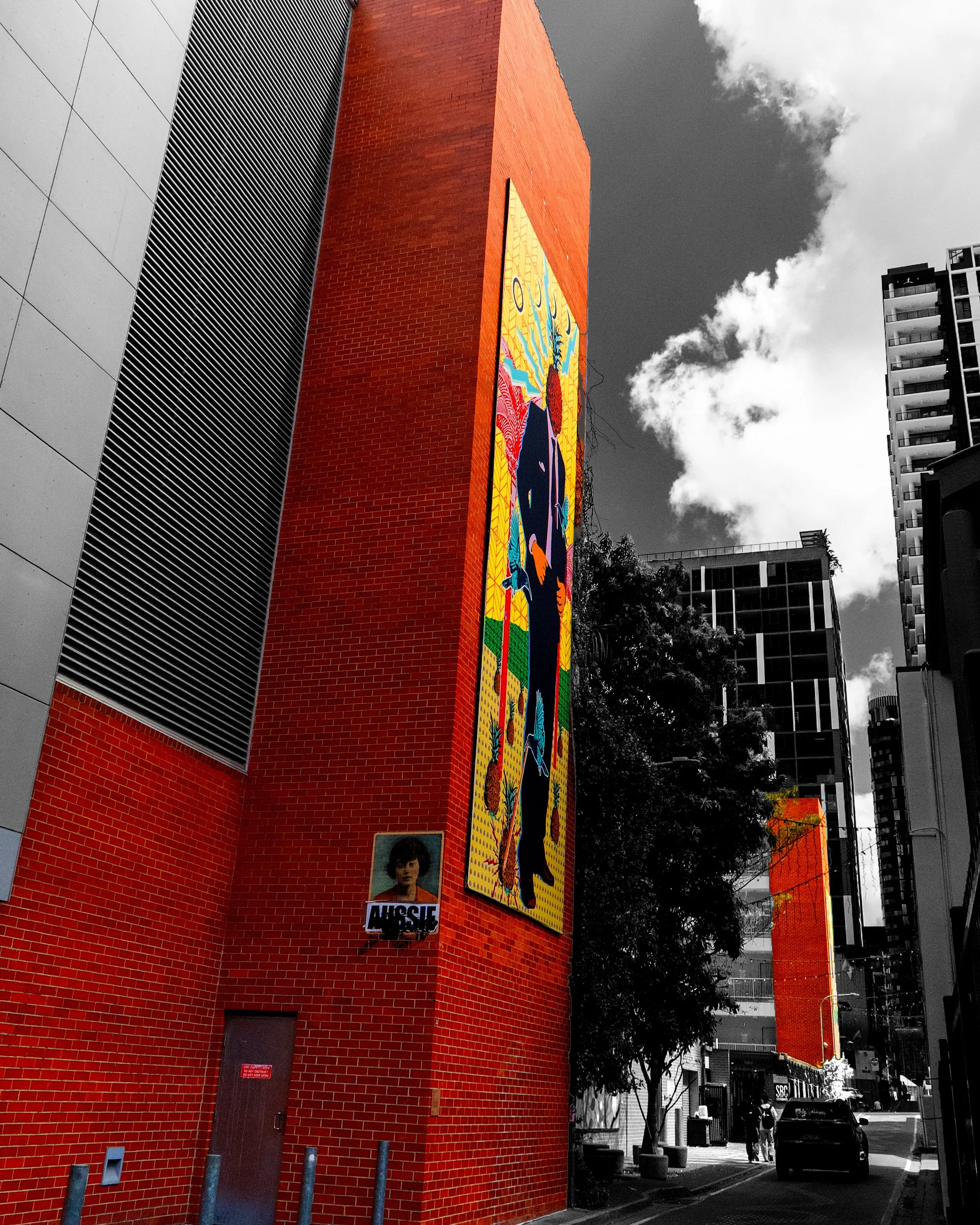 This photograph focuses on a striking orange architectural feature against a darker urban environment. The selective colour treatment emphasises its bold shape and colour, highlighting details that might otherwise go unnoticed.