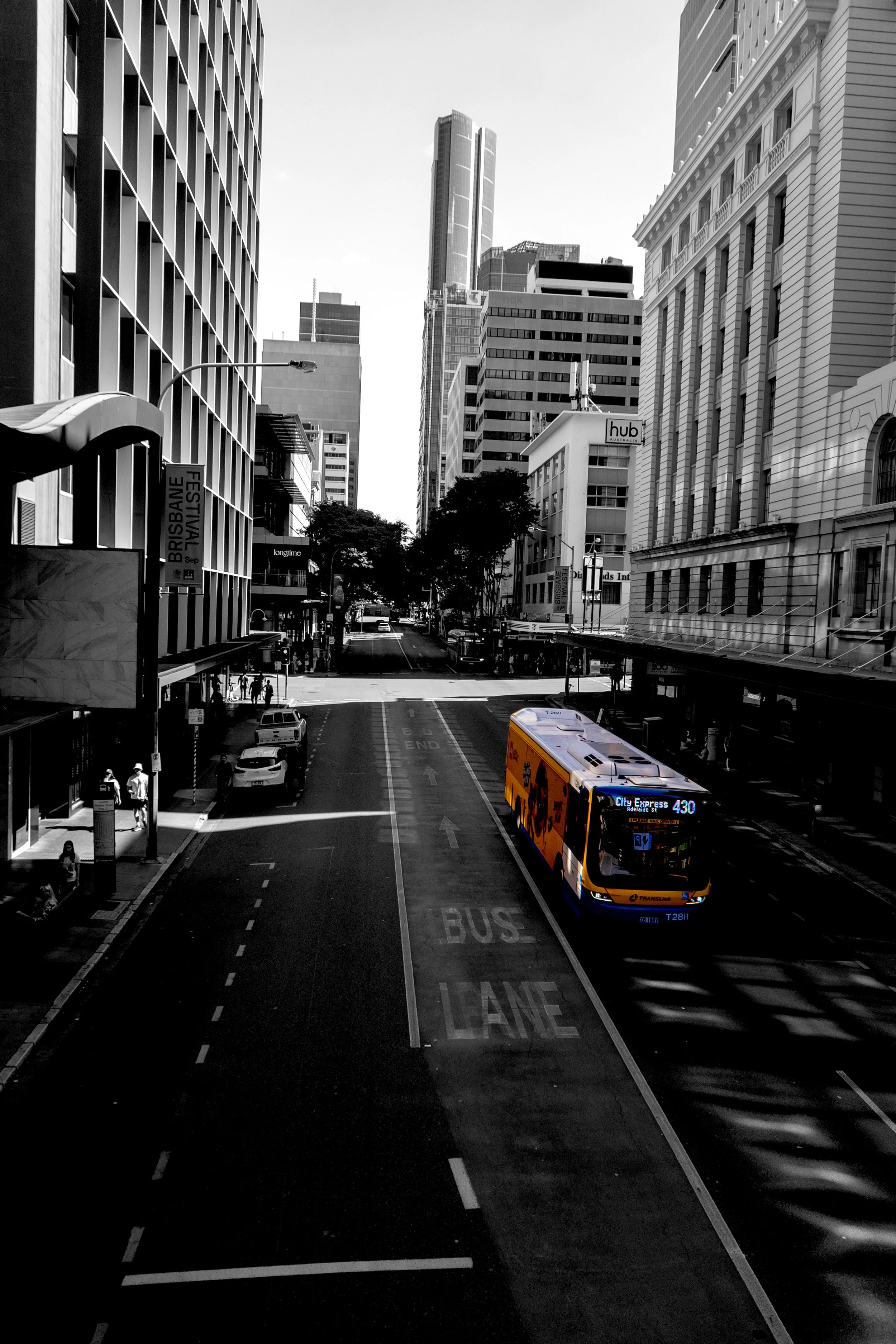 This photograph captures a city street from an elevated perspective, using architectural lines to guide the viewer's eye towards a brightly coloured vehicle. The contrast between the dark surroundings and selective colour creates a sense of movement 