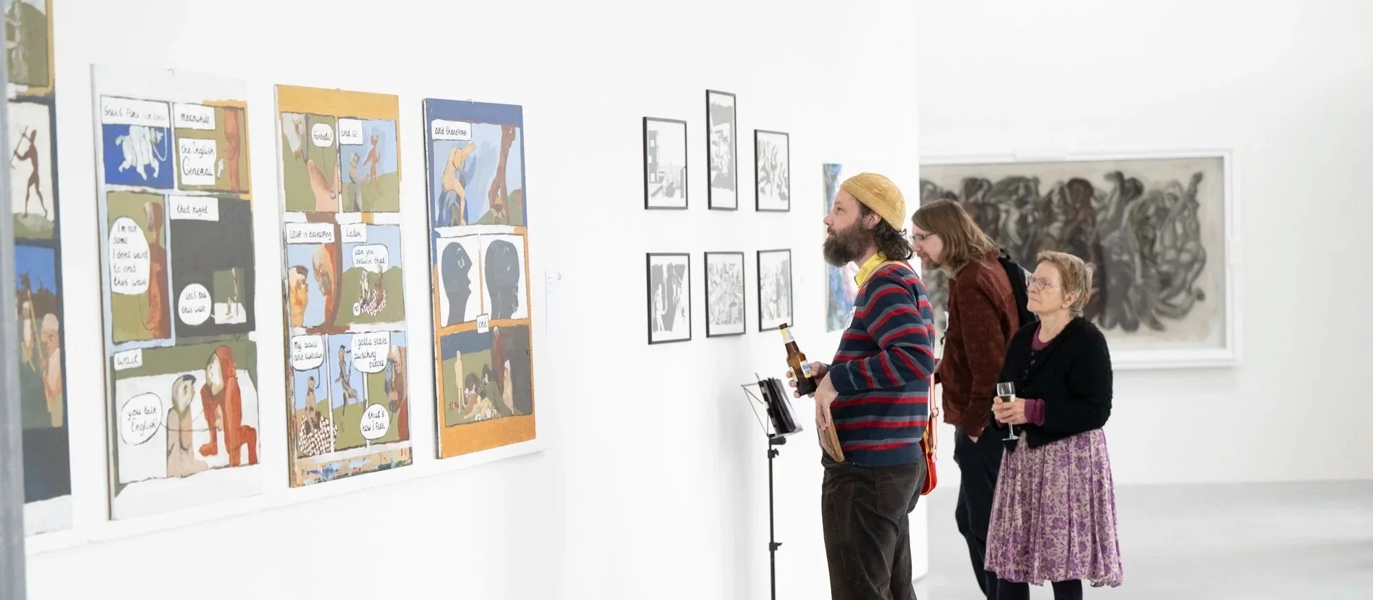Drie mensen bekijken kunstwerken in een galerie.