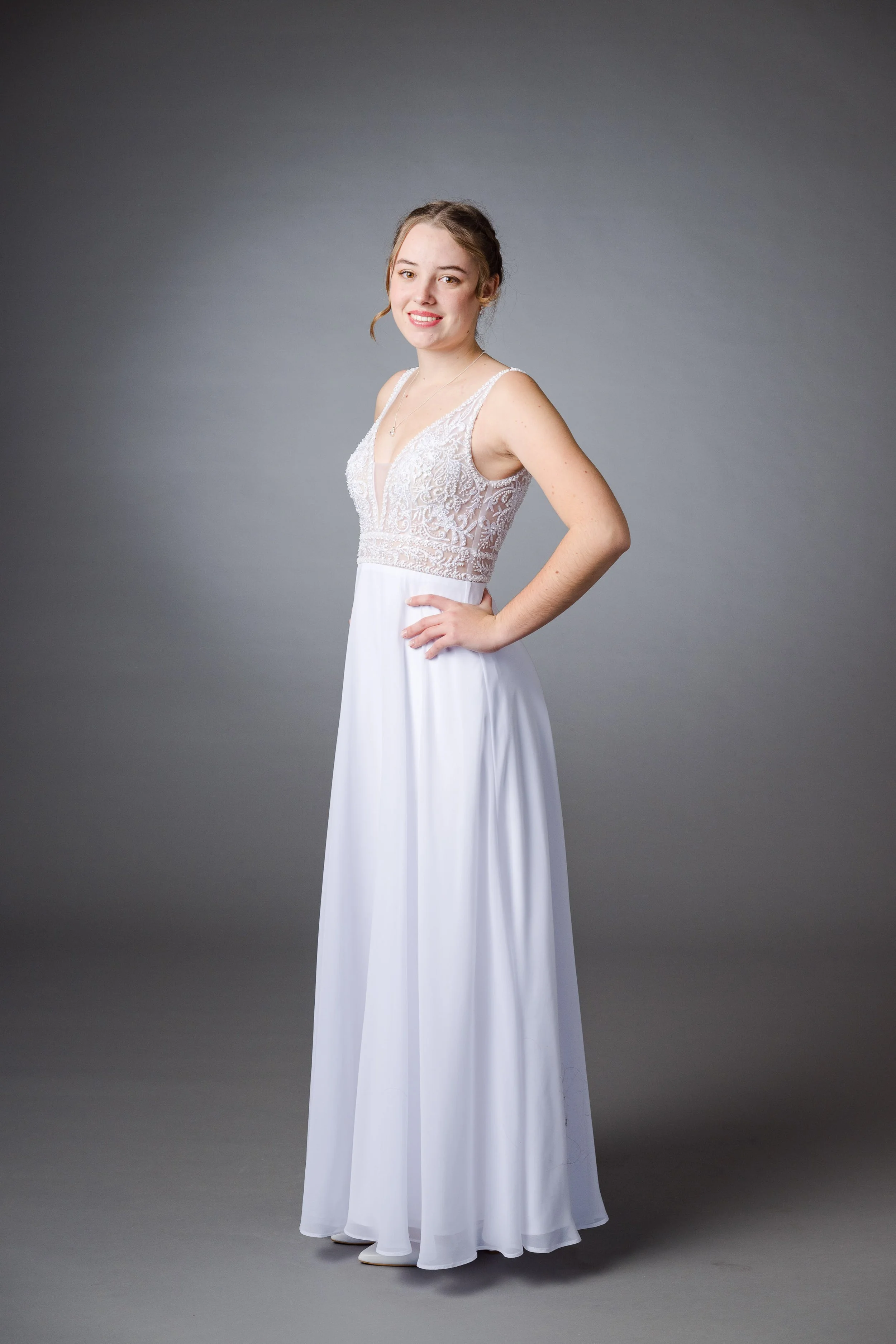 Junge Frau in weißem Brautkleid vor grauem Hintergrund.
