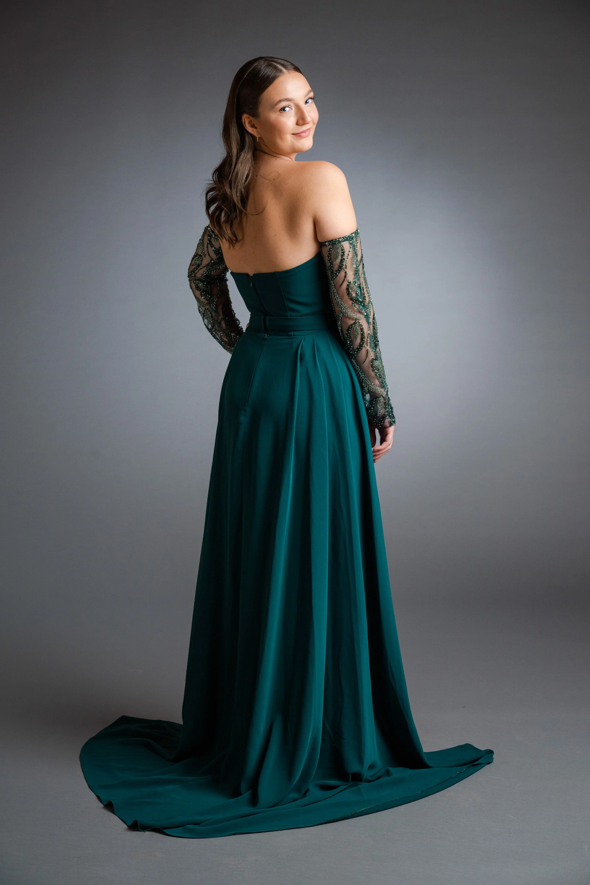 Frau in einem eleganten, grünen Abendkleid mit transparenten, verzierter Ärmel, lächelnd und in eine leichte Drehung versetzt
