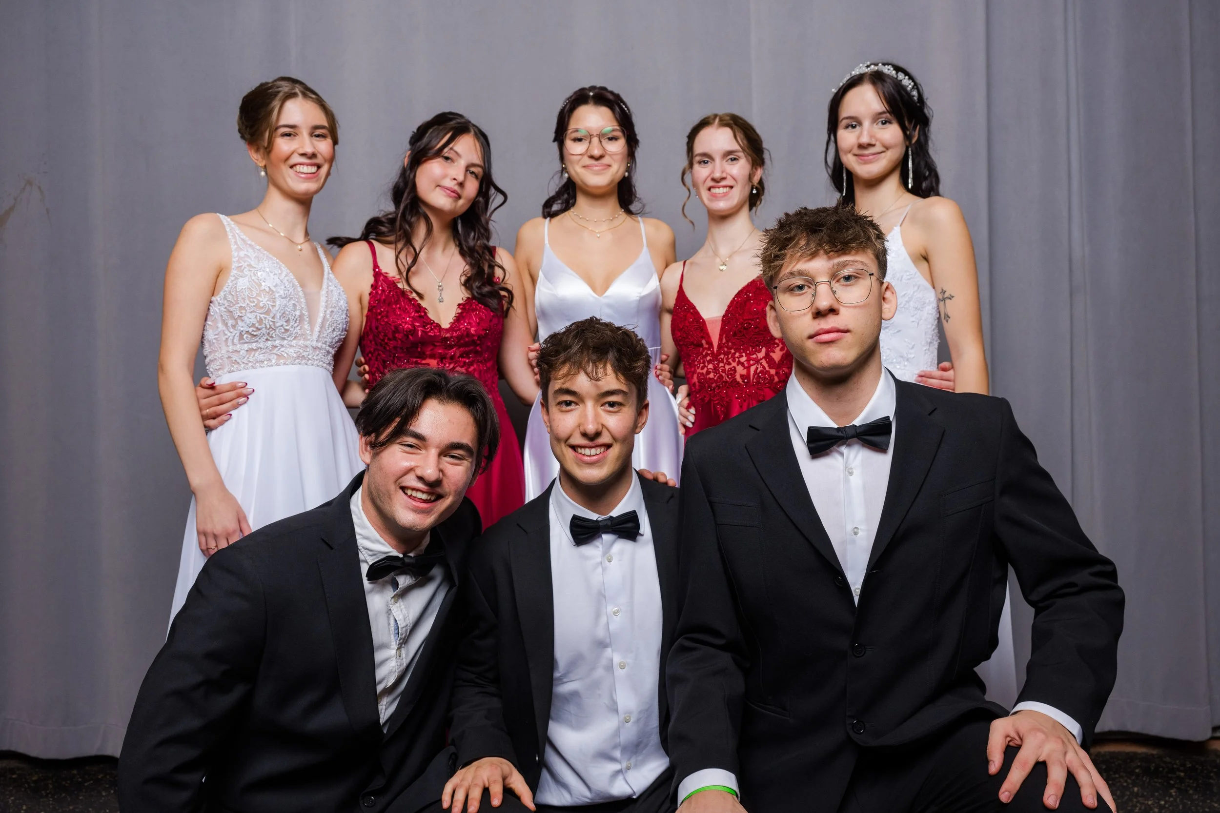 Eine Gruppe junger Menschen in formeller Kleidung, die für ein Foto posieren, vor einem grauen Vorhang.