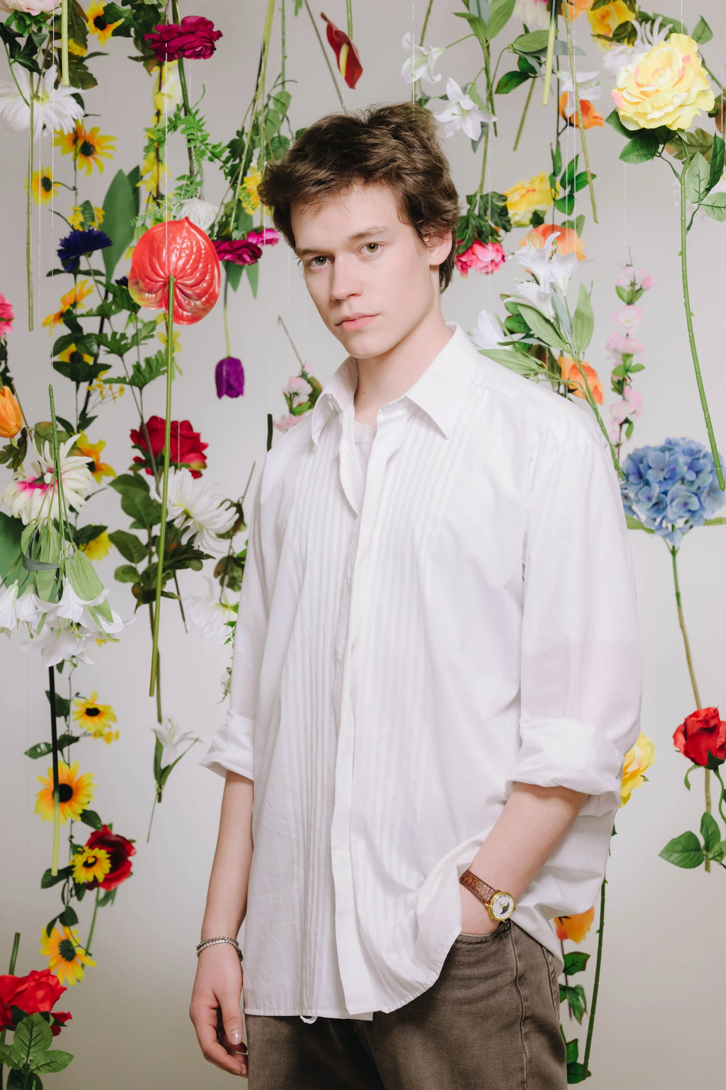 Junge Männerportrait vor einer bunten Blumenwand.