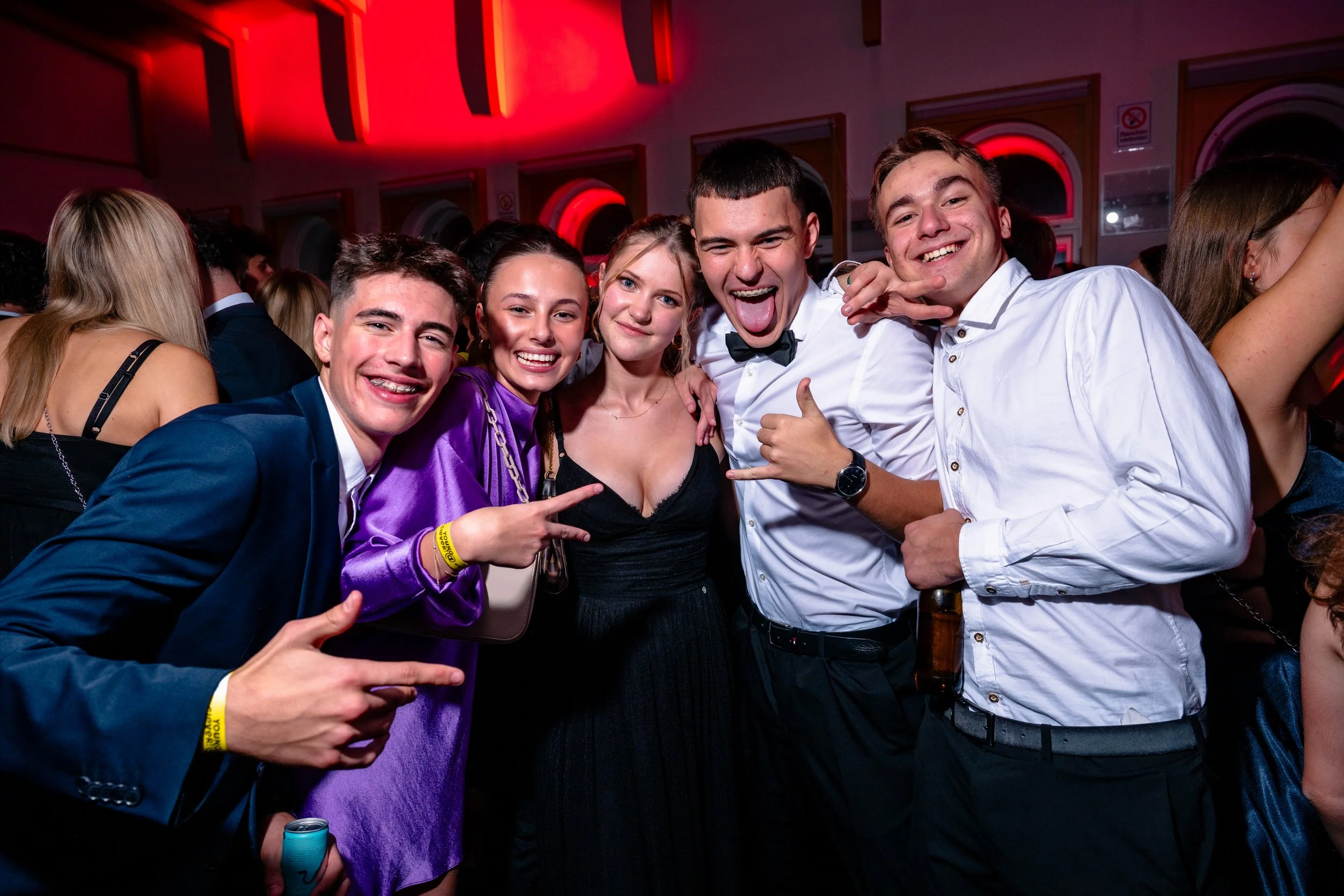 Grupp von jungen Menschen, die bei einer Feier oder einem Ball in festlicher Kleidung lachen und Spaß haben.