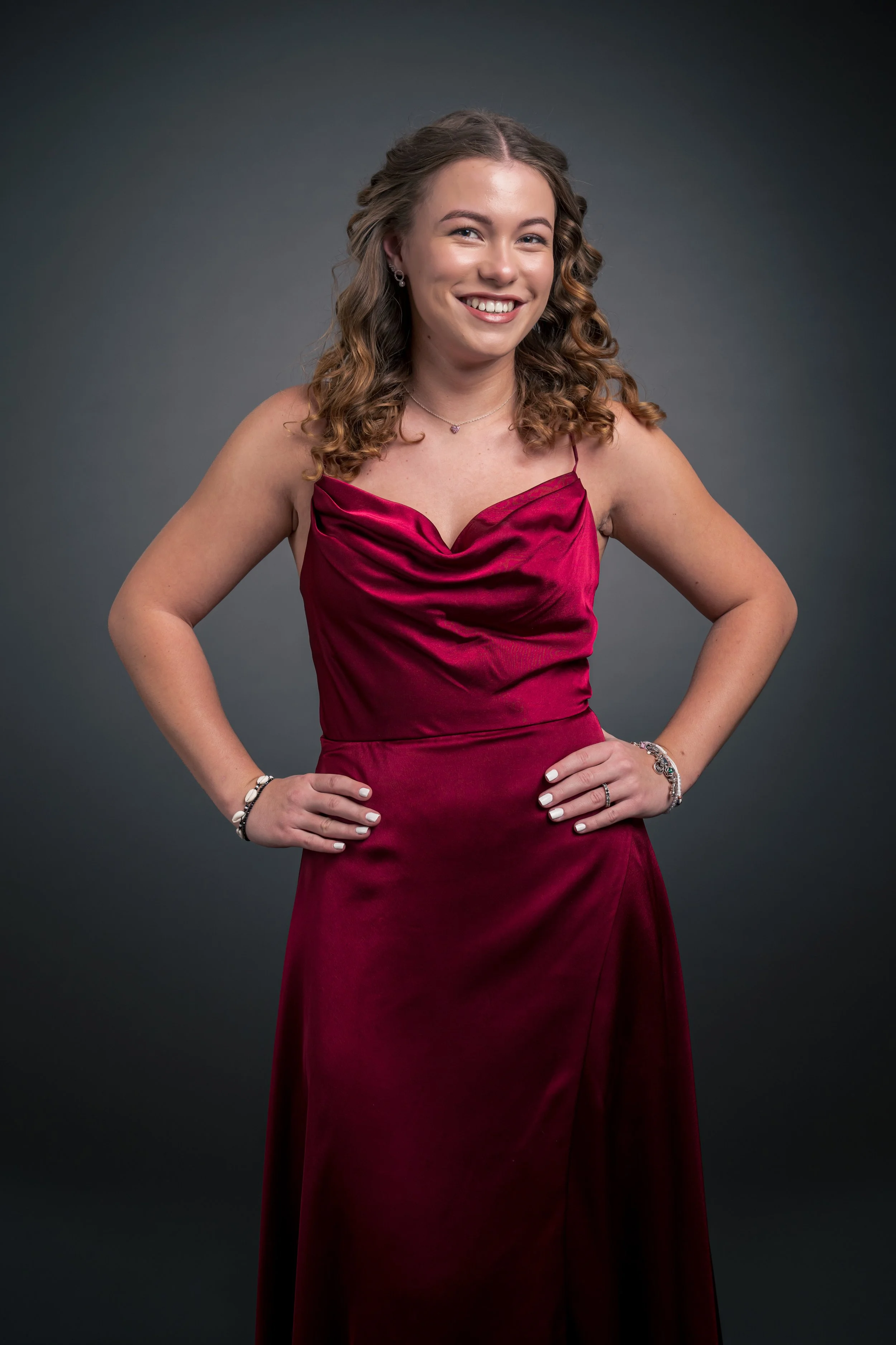 Eine junge Frau trägt ein rotes Abendkleid und lächelt vor einem grauen Hintergrund.