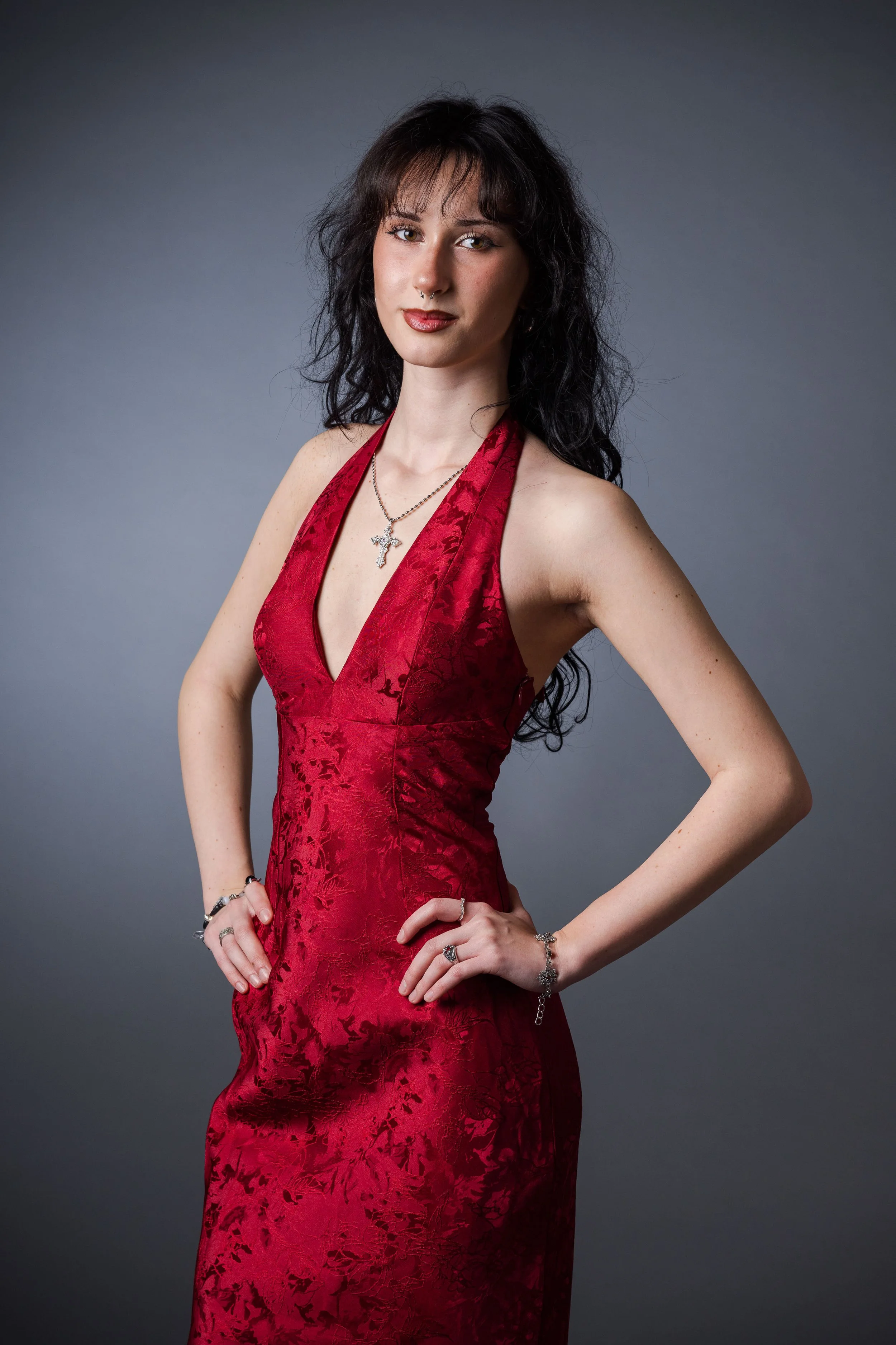 Junge Frau in rotem Kleid mit Schmuck posiert vor grauem Hintergrund.