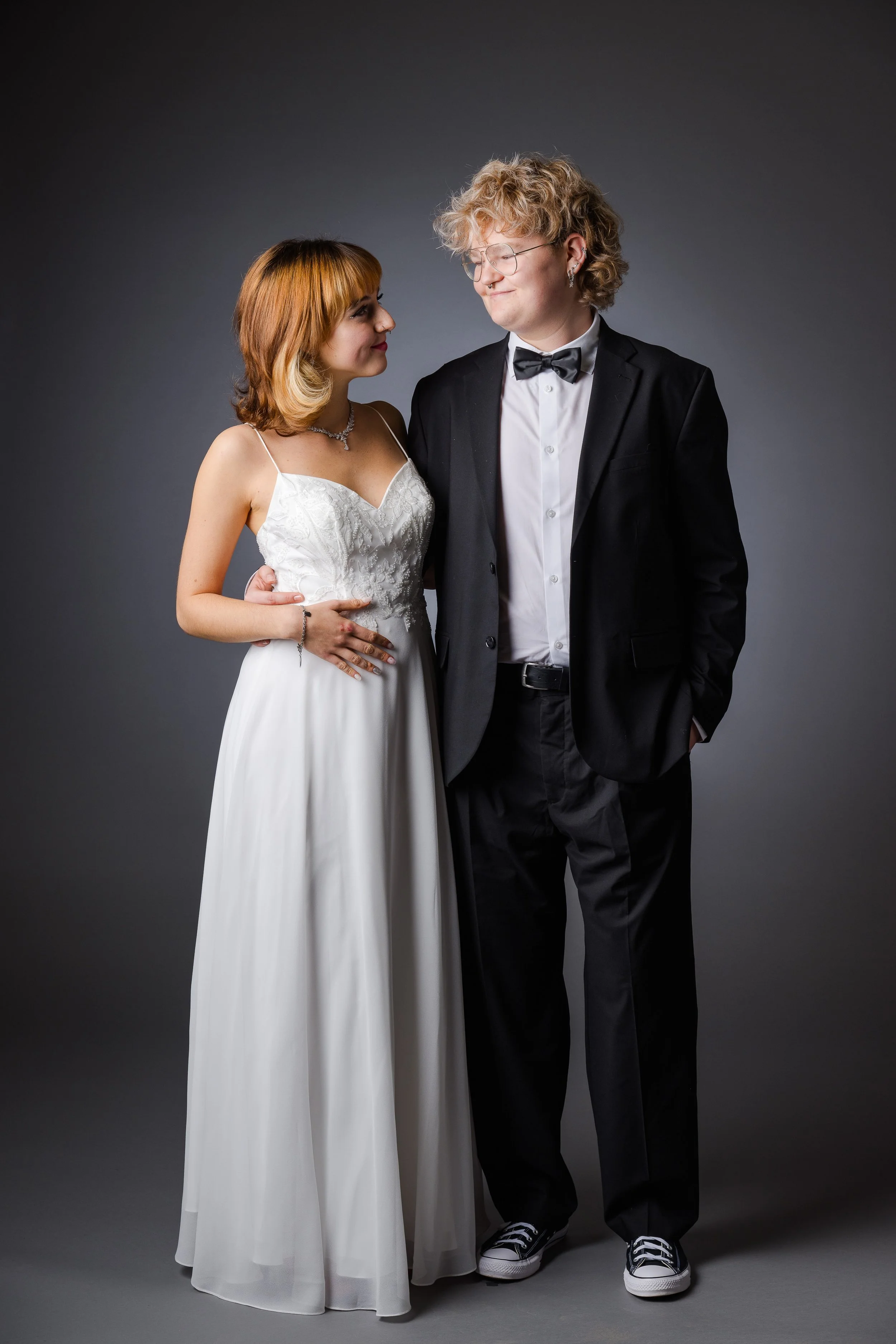 Ein junges Paar bei einer Hochzeit, das Brautkleid und Anzug trägt, auf grauem Hintergrund.