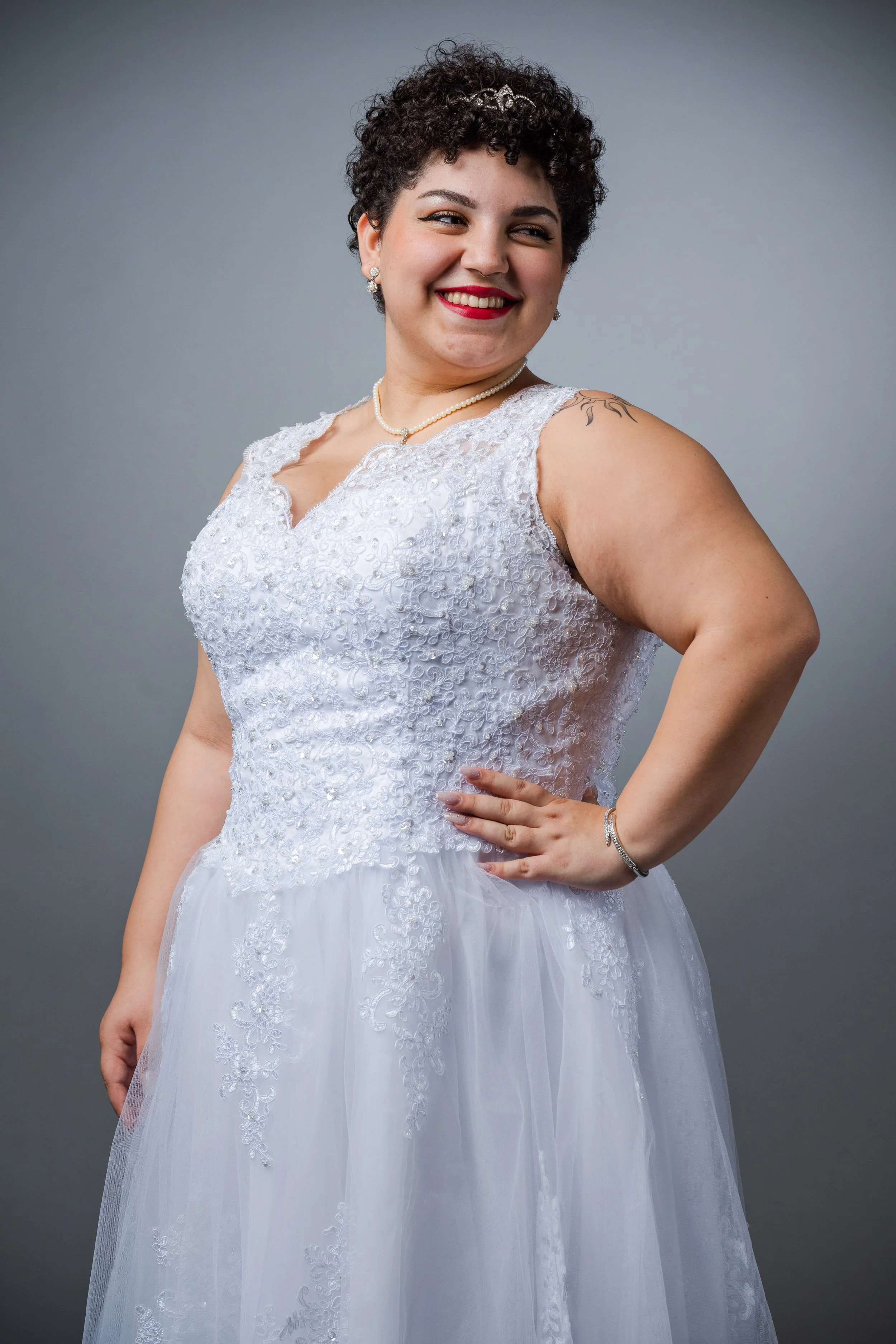 Frau in weißem Hochzeitskleid, lächelnd, vor grauem Hintergrund.