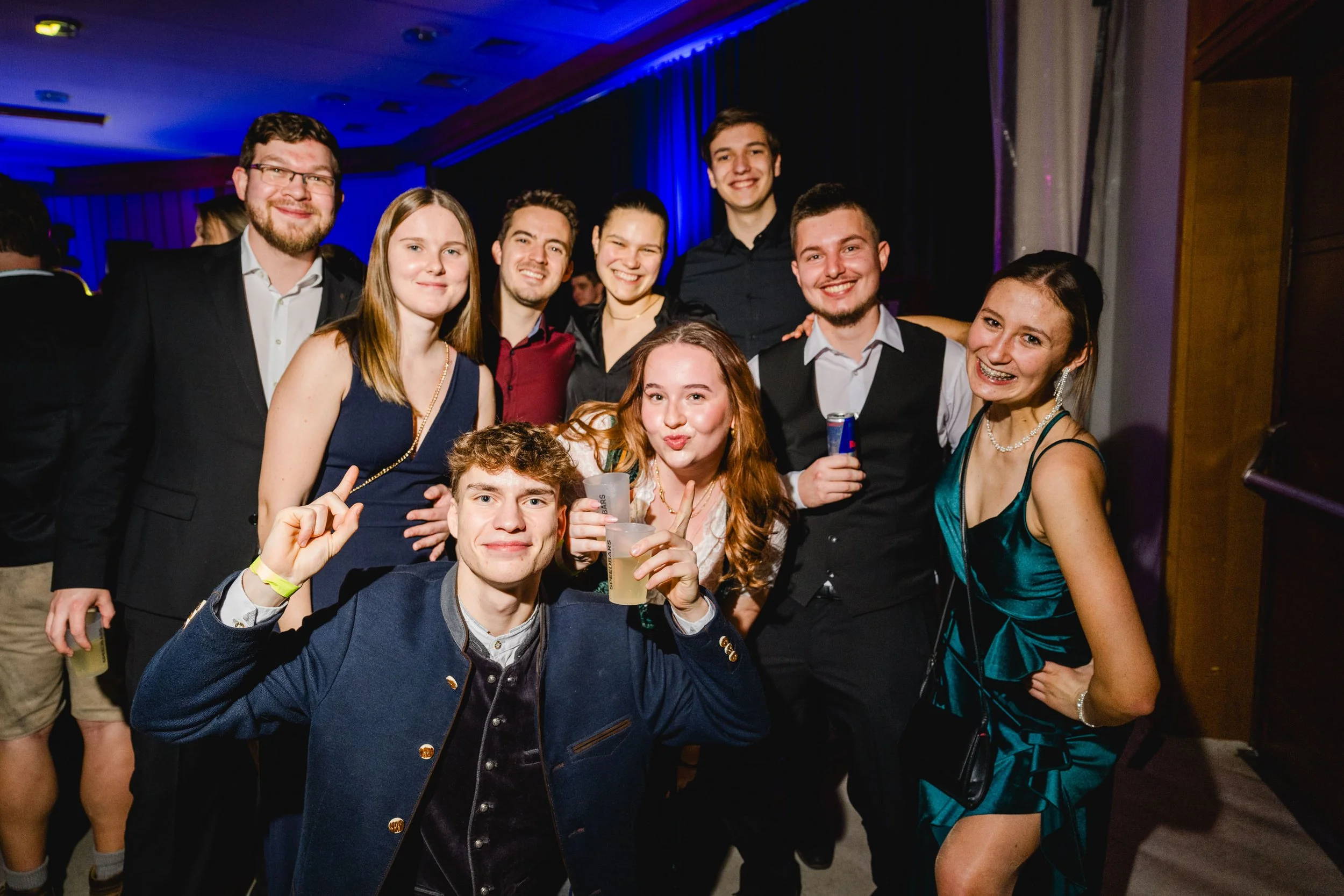Gruppe junger Menschen beim Feiern auf einer Party, lachend und Getränke haltend, in einem festlich beleuchteten Raum.