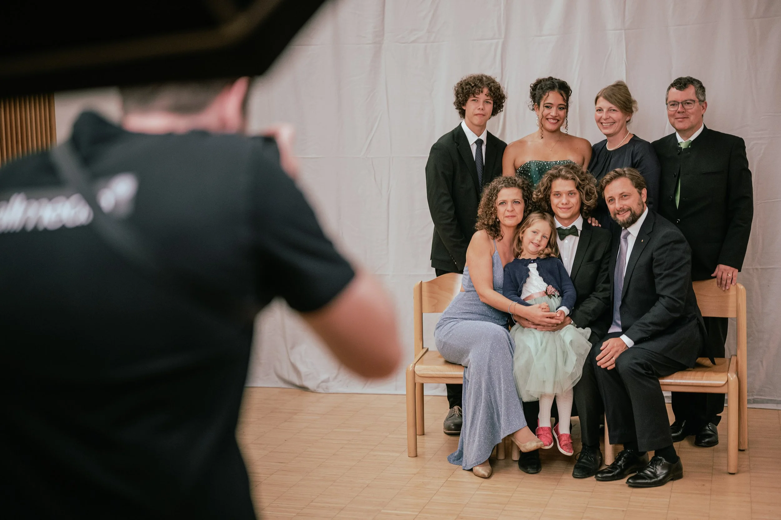 Gruppenfoto bei einer formellen Veranstaltung mit sieben Erwachsenen und einem Kind, aufgenommen vor einem weißen Hintergrund.