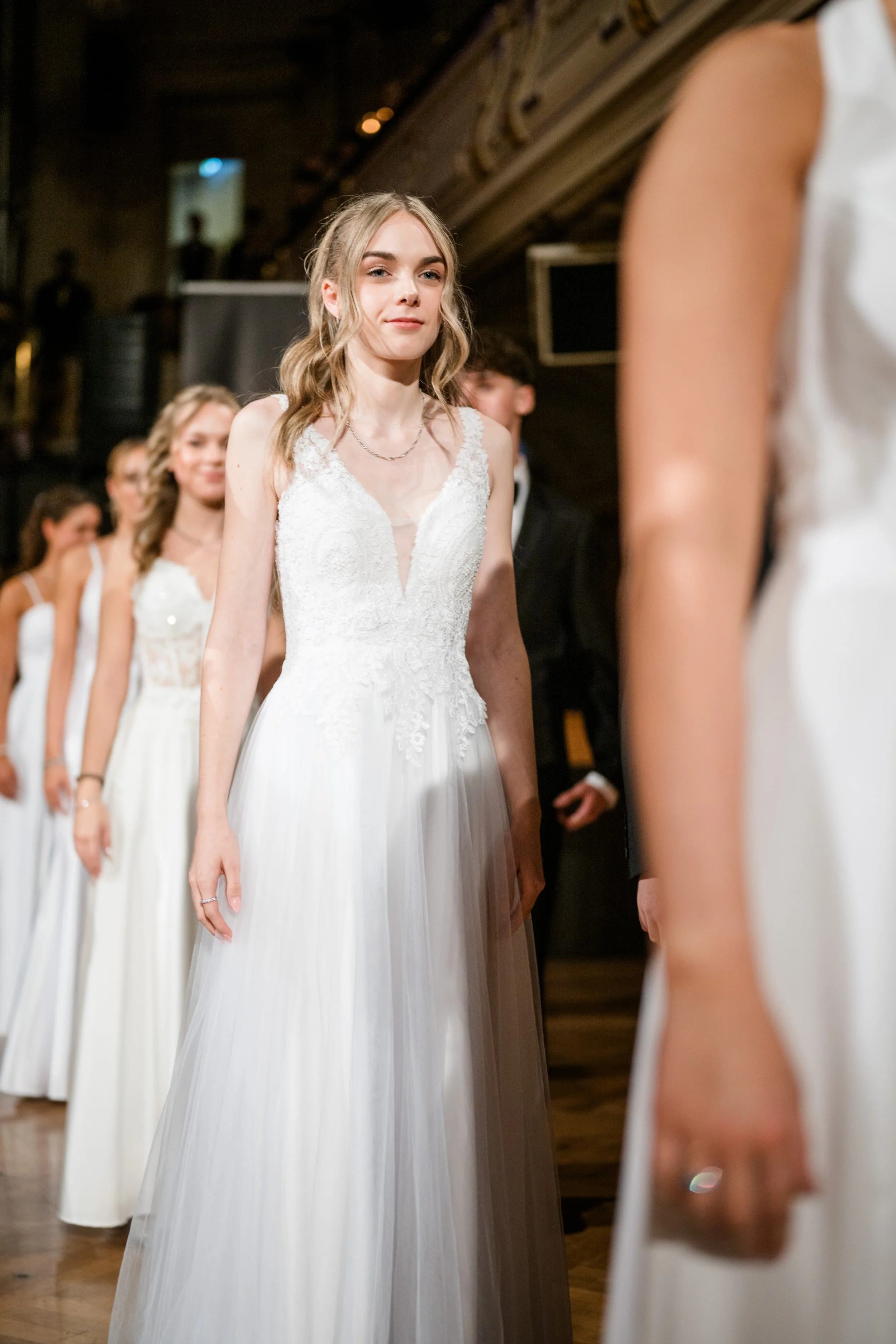 Eine junge Frau in einem weißen Brautkleid steht in einer Reihe mit anderen Frauen in weißen Brautkleidern während einer Hochzeitszeremonie.