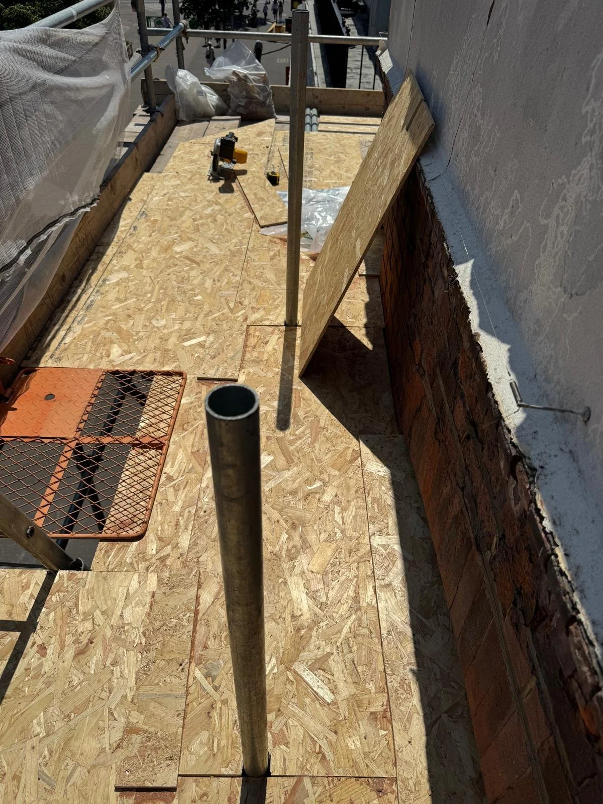 Timber boards protecting the flat roof beside the parapet wall rebuild in Sutton, with scaffolding and sheeting around the work area