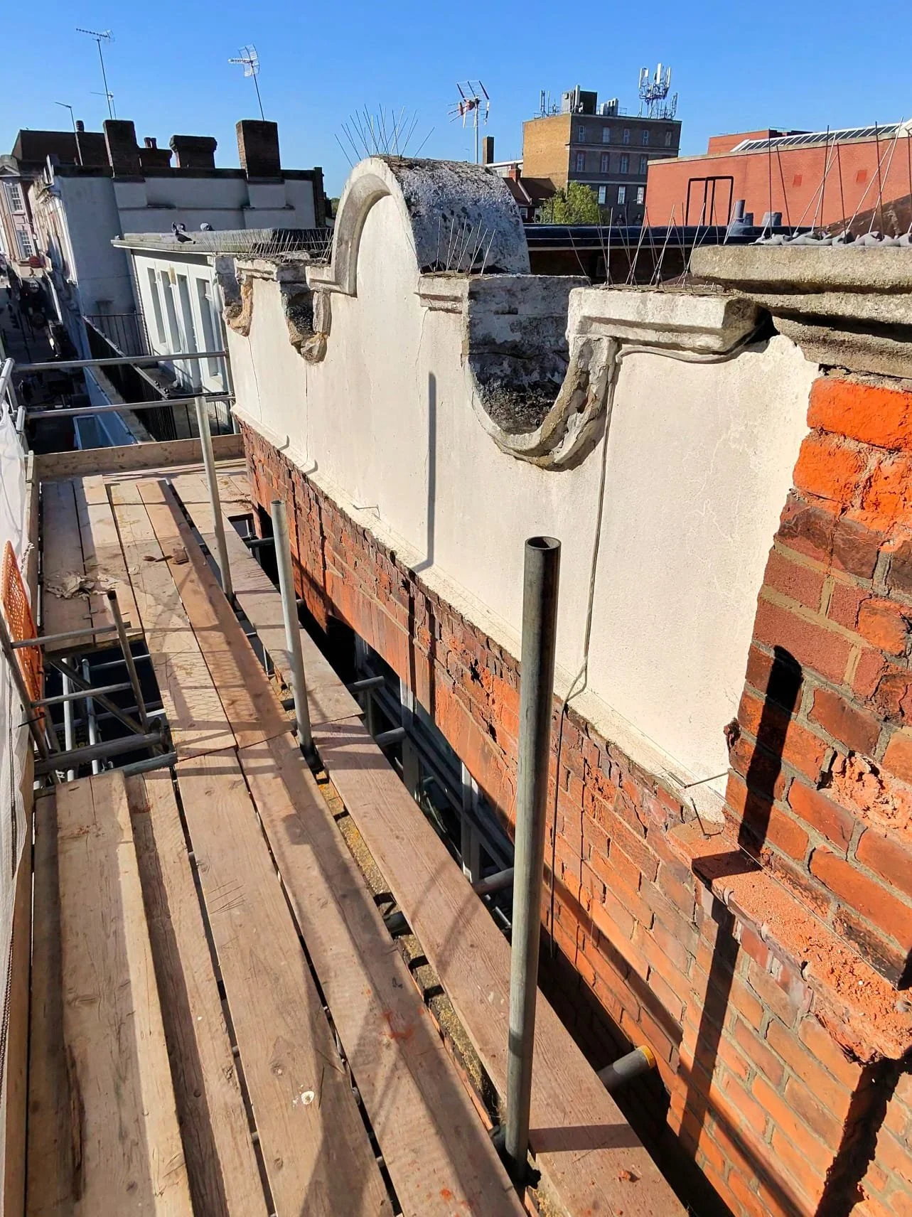 Ornamental rendered parapet details exposed above stripped brickwork during the Sutton wall repair, seen from the scaffold walkway