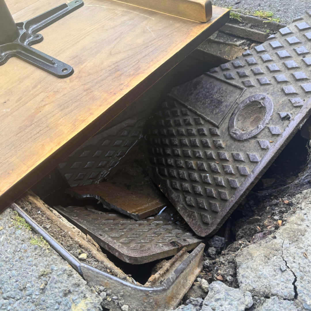 Cracked, collpased, and broken man hole cover in the middle of a pub car park that was dangerous to patrons and staff