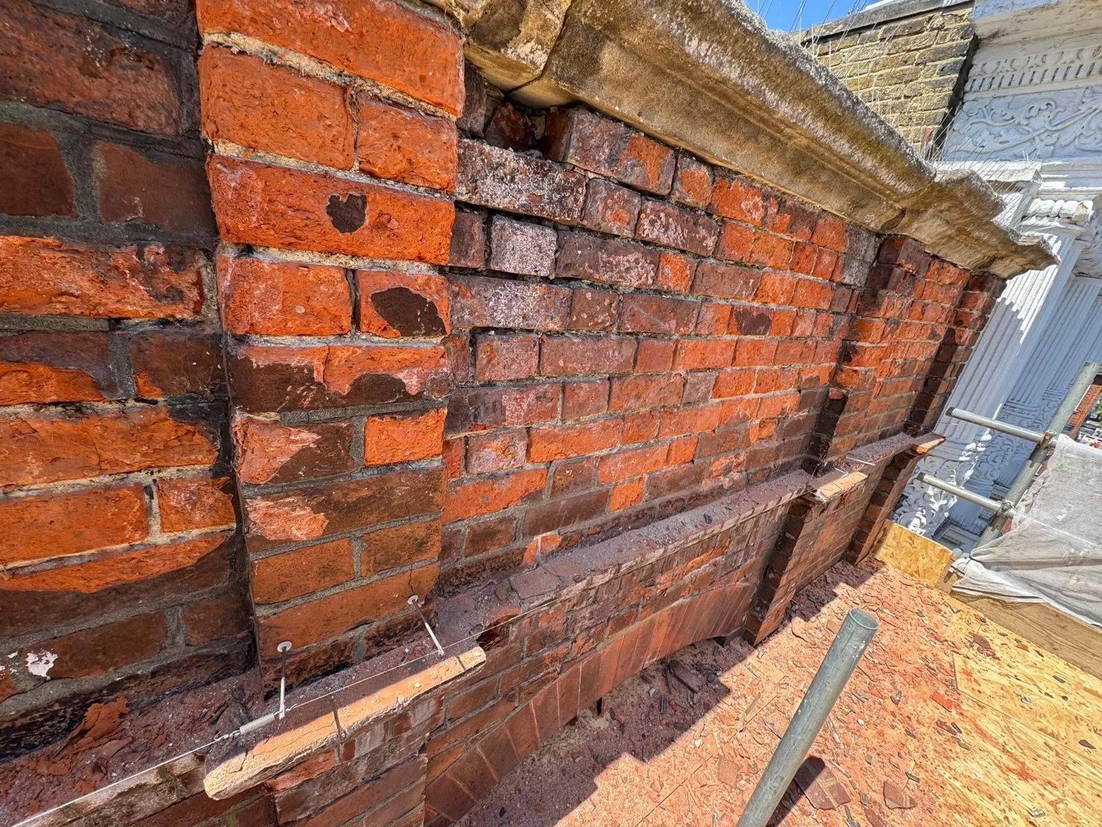 Weathered brick parapet wall in Sutton with coping stones removed and steel reinforcement bars fitted during repair by Medlec