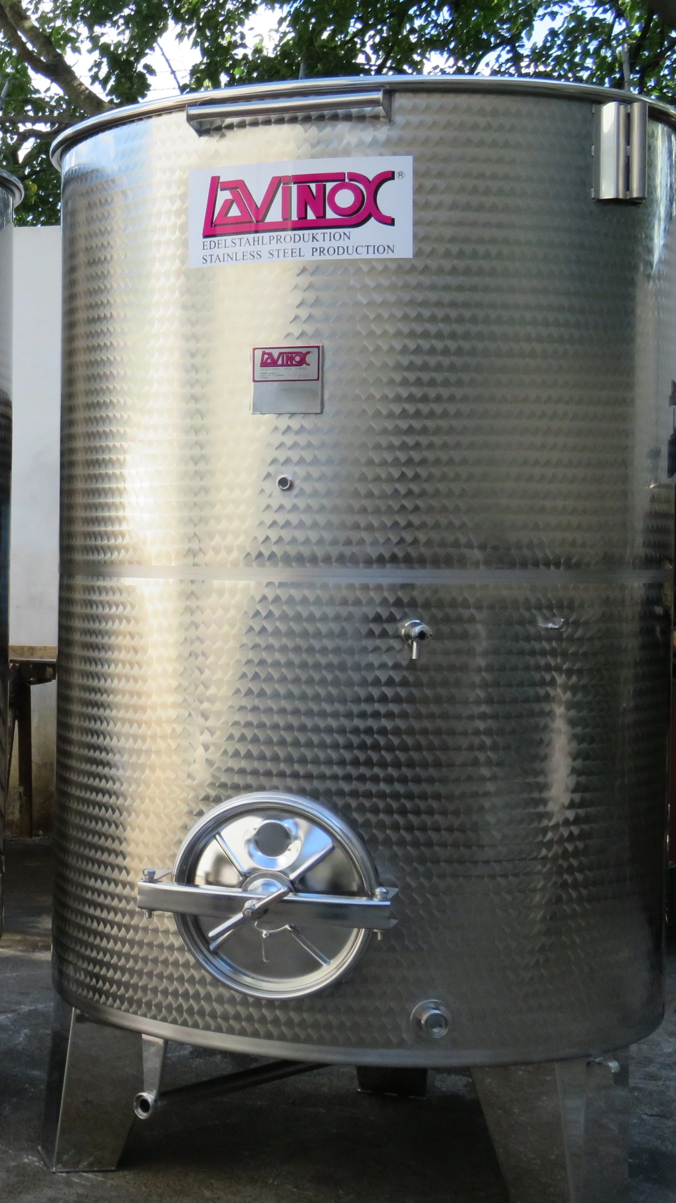 A large stainless steel industrial beverage tank with a textured surface, labeled with the brand name 'Lavinox,' used for wine production.