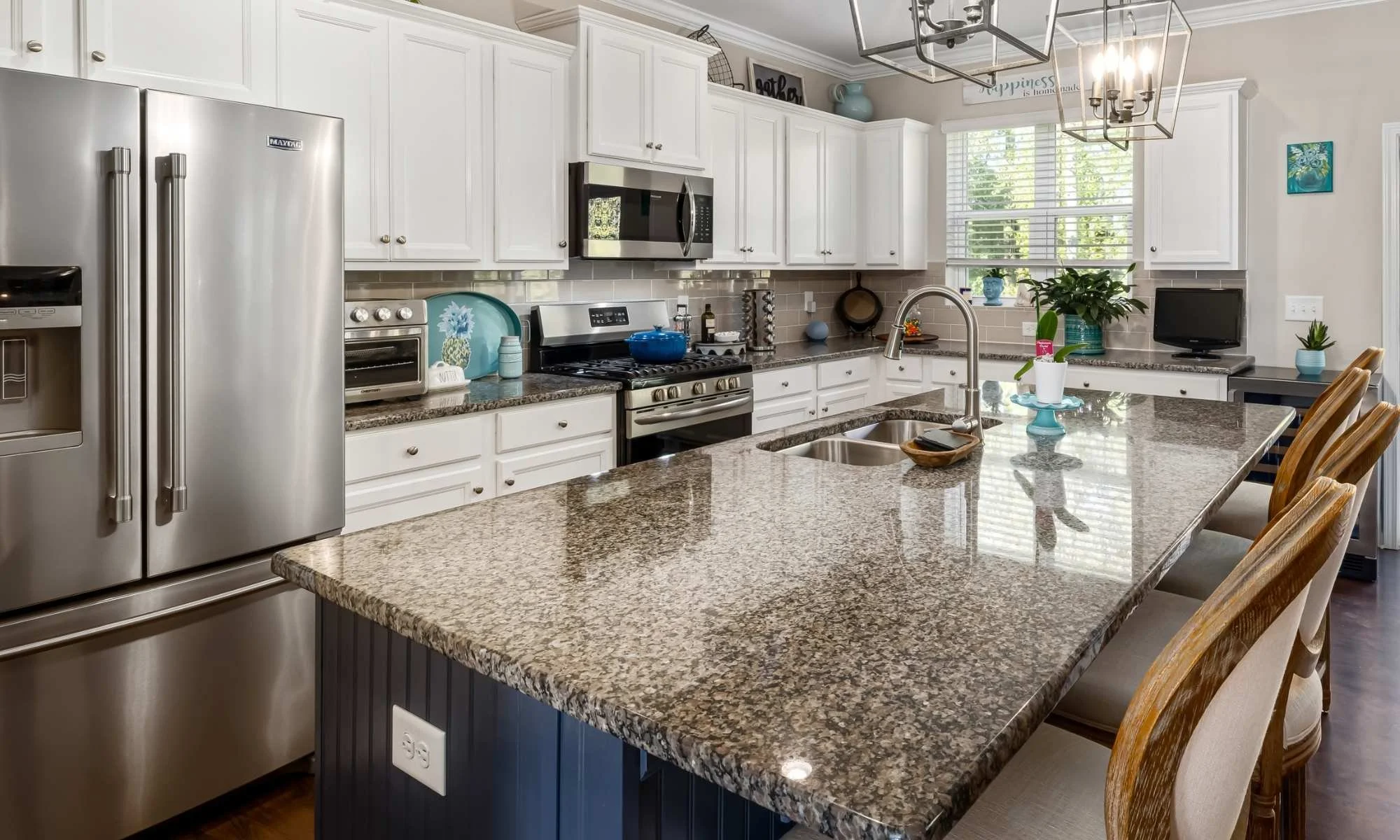 Bright kitchen with granite countertops, large center island, stainless appliances, white cabinets, and teal decorative accents.  Showing professional house cleaning by Scrubbles.
