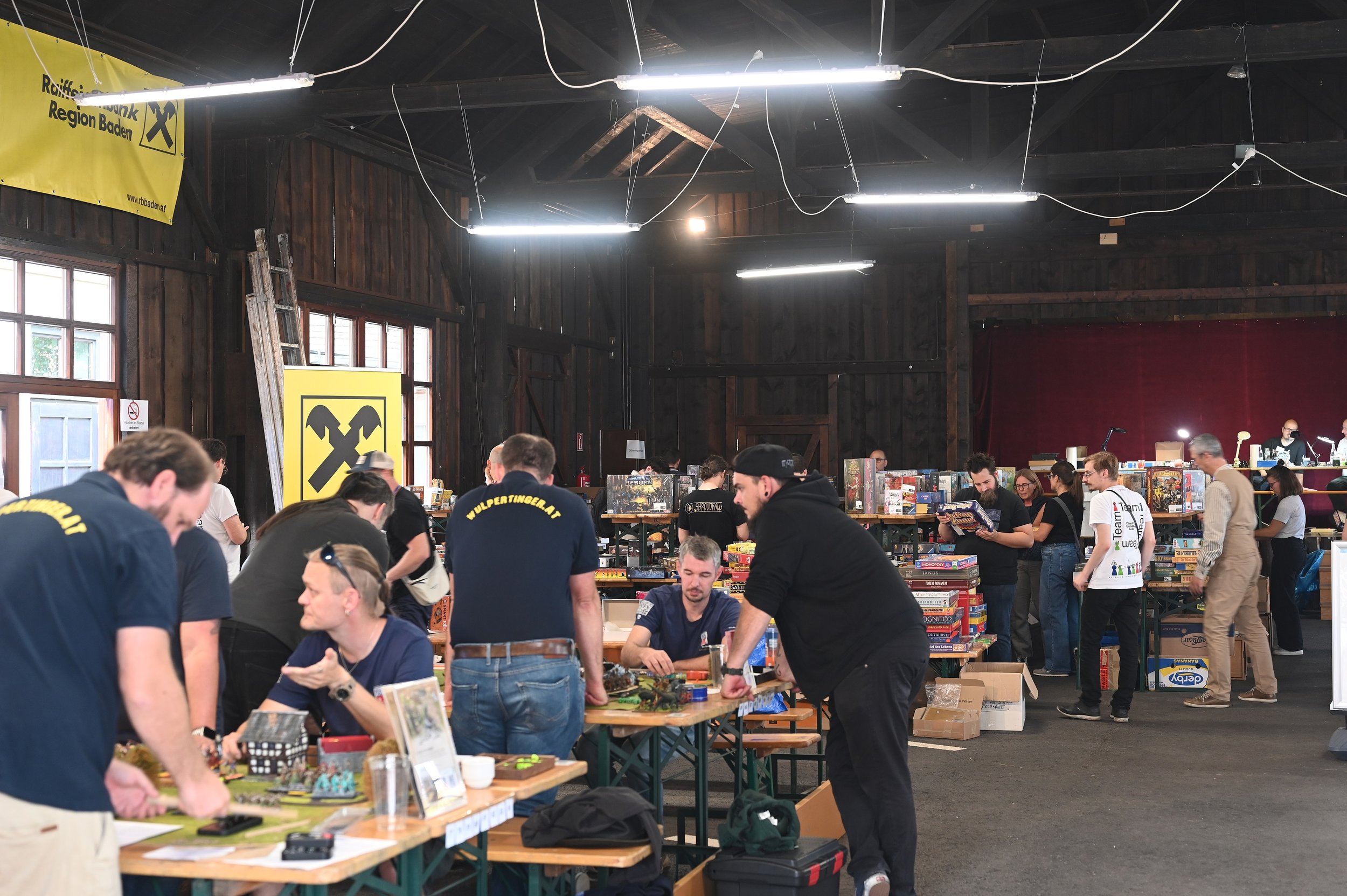 Stadl mit großen Spieletischen, Stapeln an Spielen und Malen im Hintergrund.