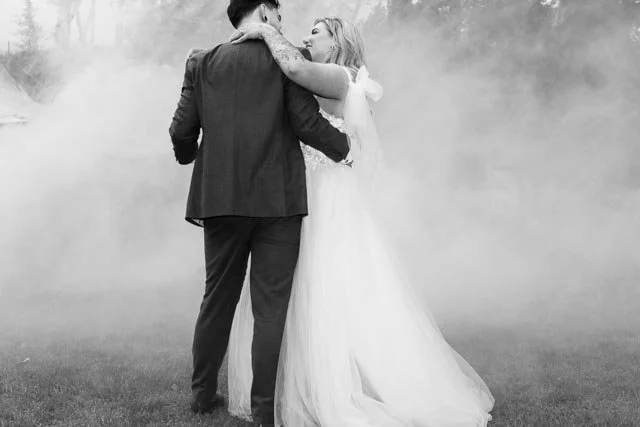 Bride and groom dancing outdoors, surrounded by fog, in black and white.