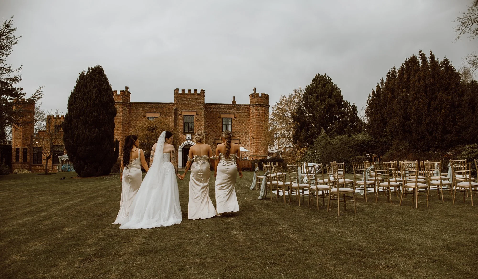 Bride and bridesmaids walking towards castle, outdoor wedding venue with chairs on lawn.
