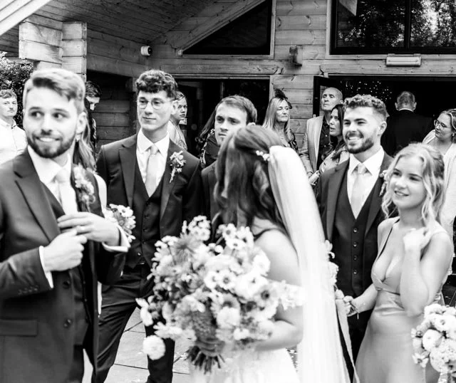 Group at wedding gathering, people in formal attire, bride holding bouquet, black and white photograph.