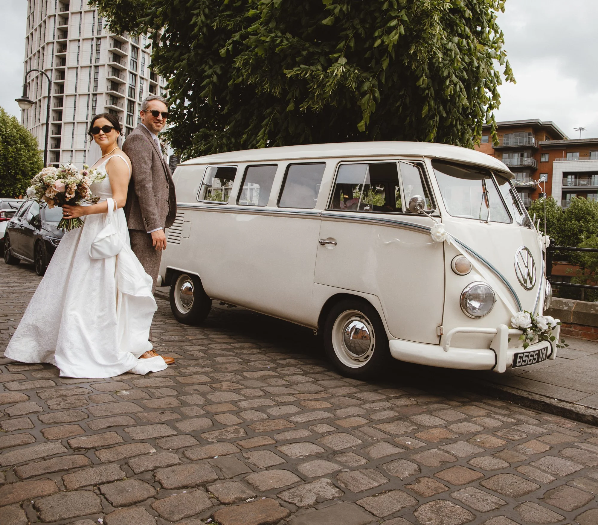 A bride and groom standing next to a vintage white Volkswagen van decorated with flowers for a wedding celebration.