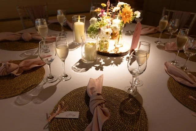 Table setting with white flowers, candles, and glasses at an event.