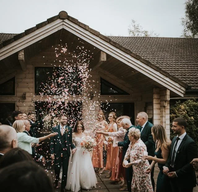 Wedding celebration with couple exiting building, surrounded by guests throwing confetti.
