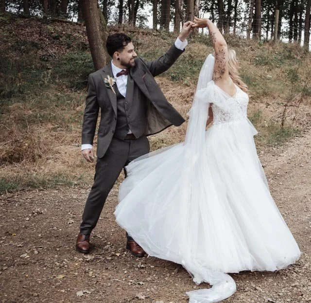 Bride and groom dancing outdoors on a wooded path.