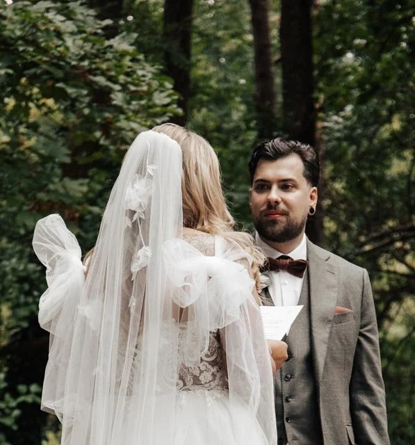 Bride and groom exchanging vows in an outdoor wedding ceremony with trees in the background.