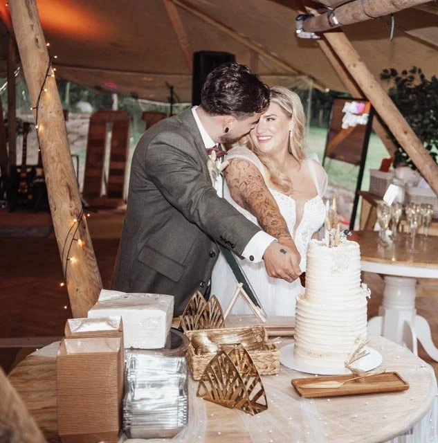 Bride and groom cutting a wedding cake under a decorated tent.