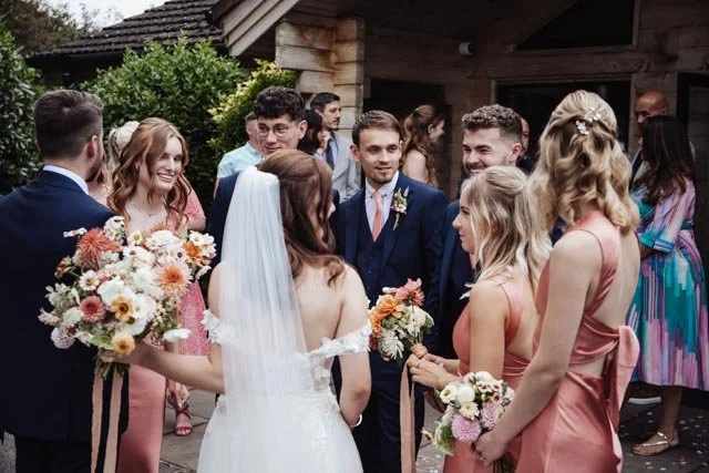 Bride and bridesmaids holding bouquets, conversing with guests at an outdoor wedding.