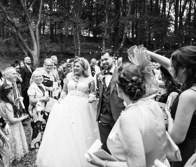 Bride and groom walking through a crowd during a confetti shower at an outdoor wedding.