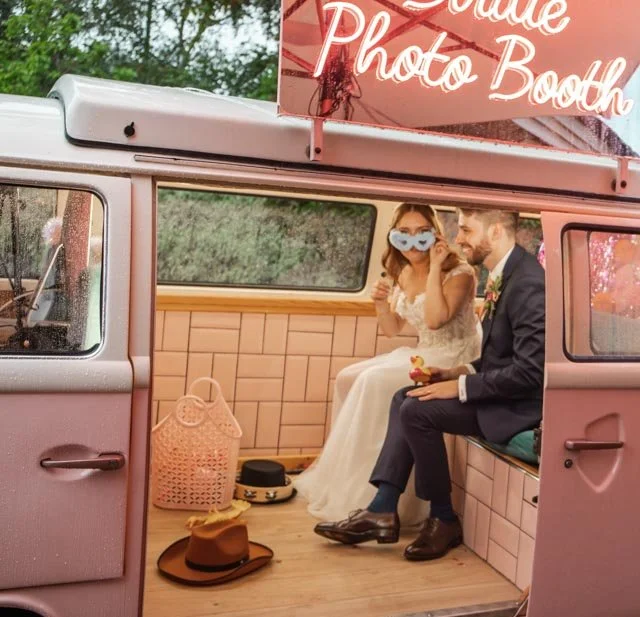 Couple inside a vintage van photo booth with neon 'Bride Photo Booth' sign