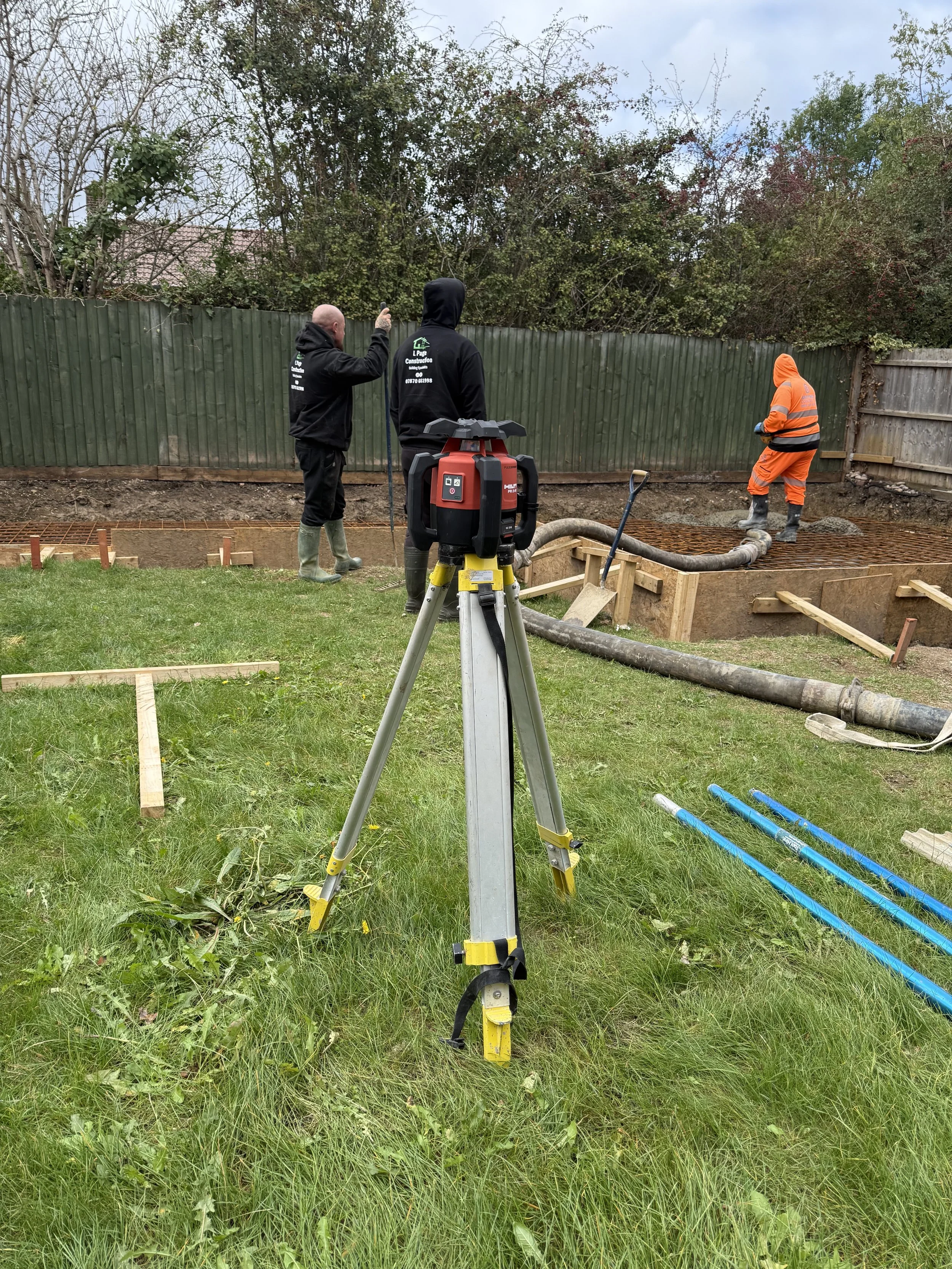 Construction workers and a supervisor working on foundation in a backyard with wood framing and construction equipment. Garage build