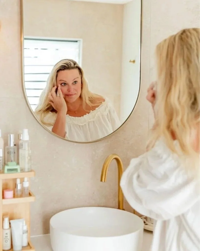 Amy smiling in the bathroom mirror as she applies eye cream after an everything shower