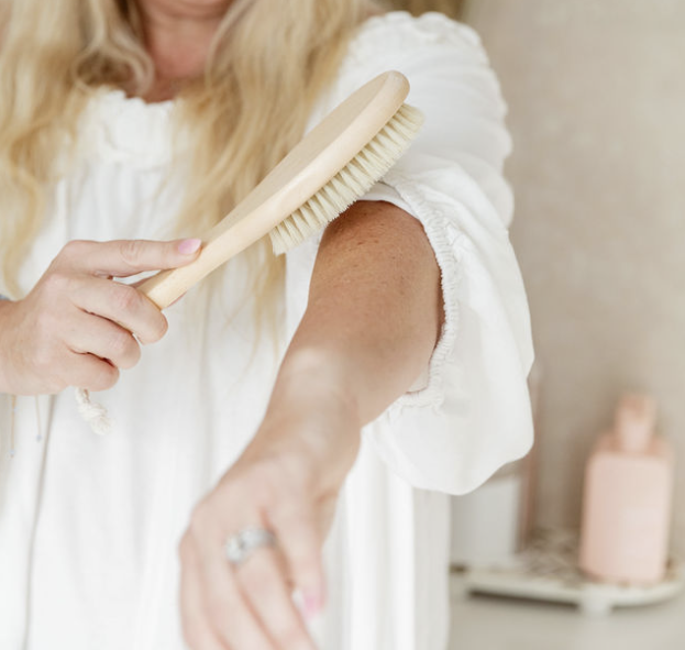 Woman dry brushing her arm with a wooden bristle brush before an everything shower