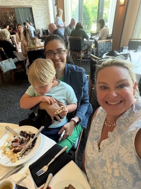 Au pair Fernanda holding a toddler at lunch with Amy at the table