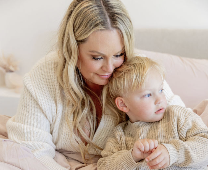 Amy Boland Hauser rests her cheek on her son Harris’ head as they sit together in cozy cream sweaters.
