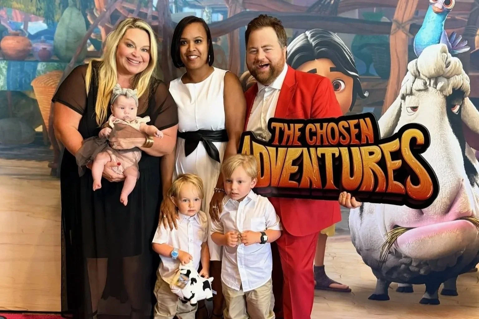 Family posing on a red carpet at "The Chosen Adventures" event photo backdrop.