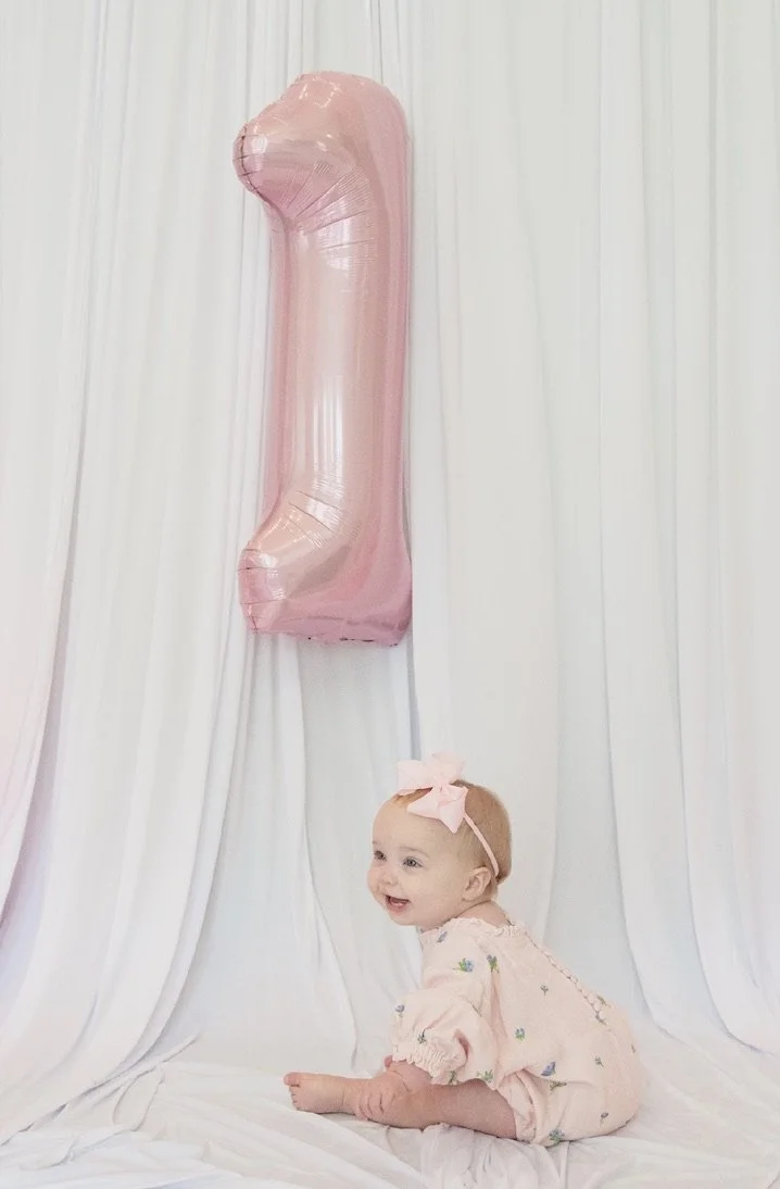 Isla Grace looking up at a pink number one balloon at her sweet one birthday party