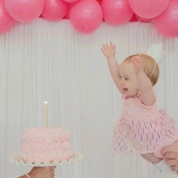 Isla Grace lifted in the air as her pink rosette smash cake is revealed with a lit candle
