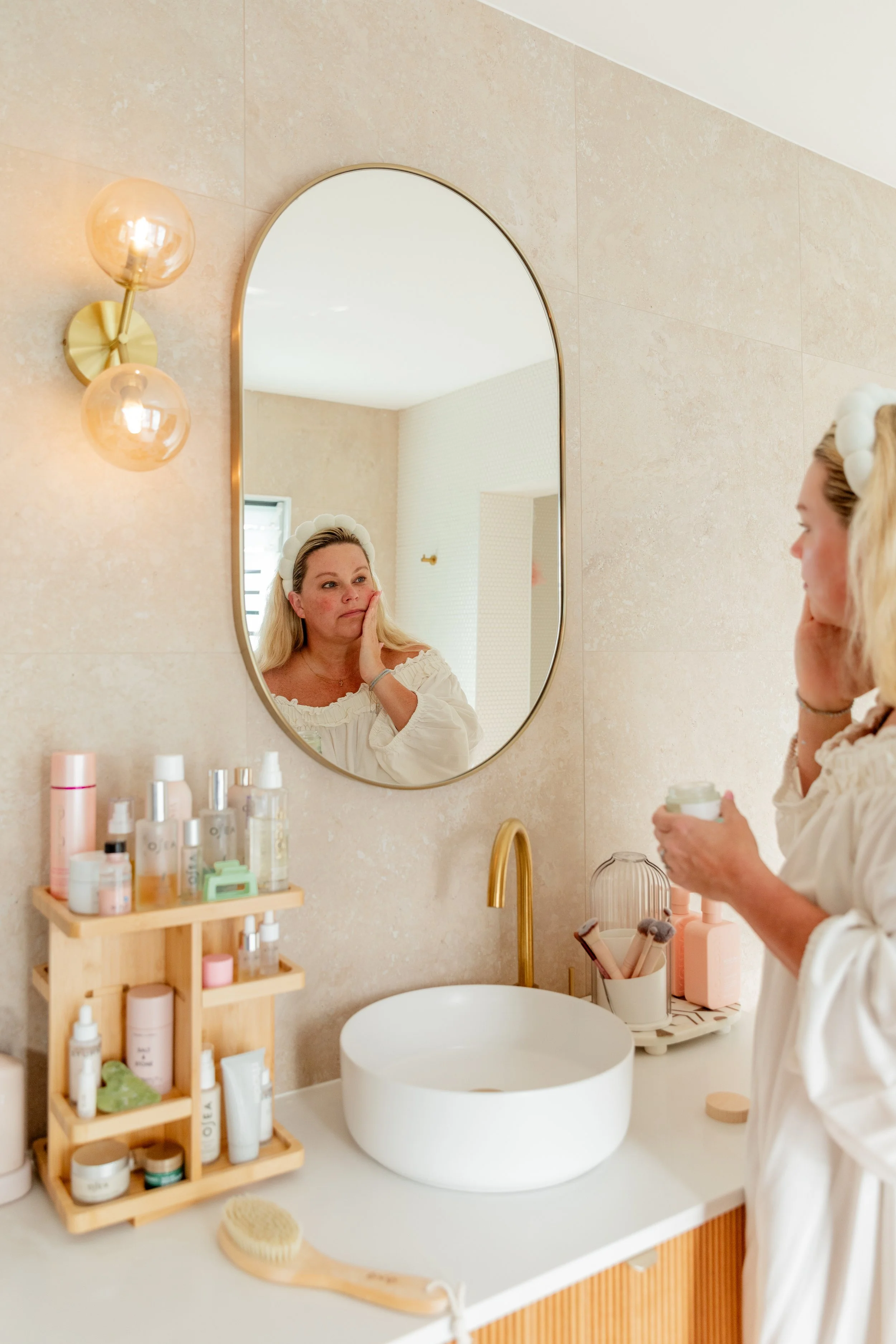 Amy in a headband applying face cream in a bathroom mirror as part of her post everything shower routine