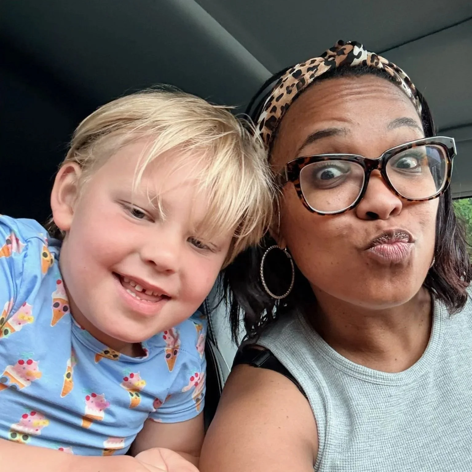 Young boy and woman making silly faces together in a car.