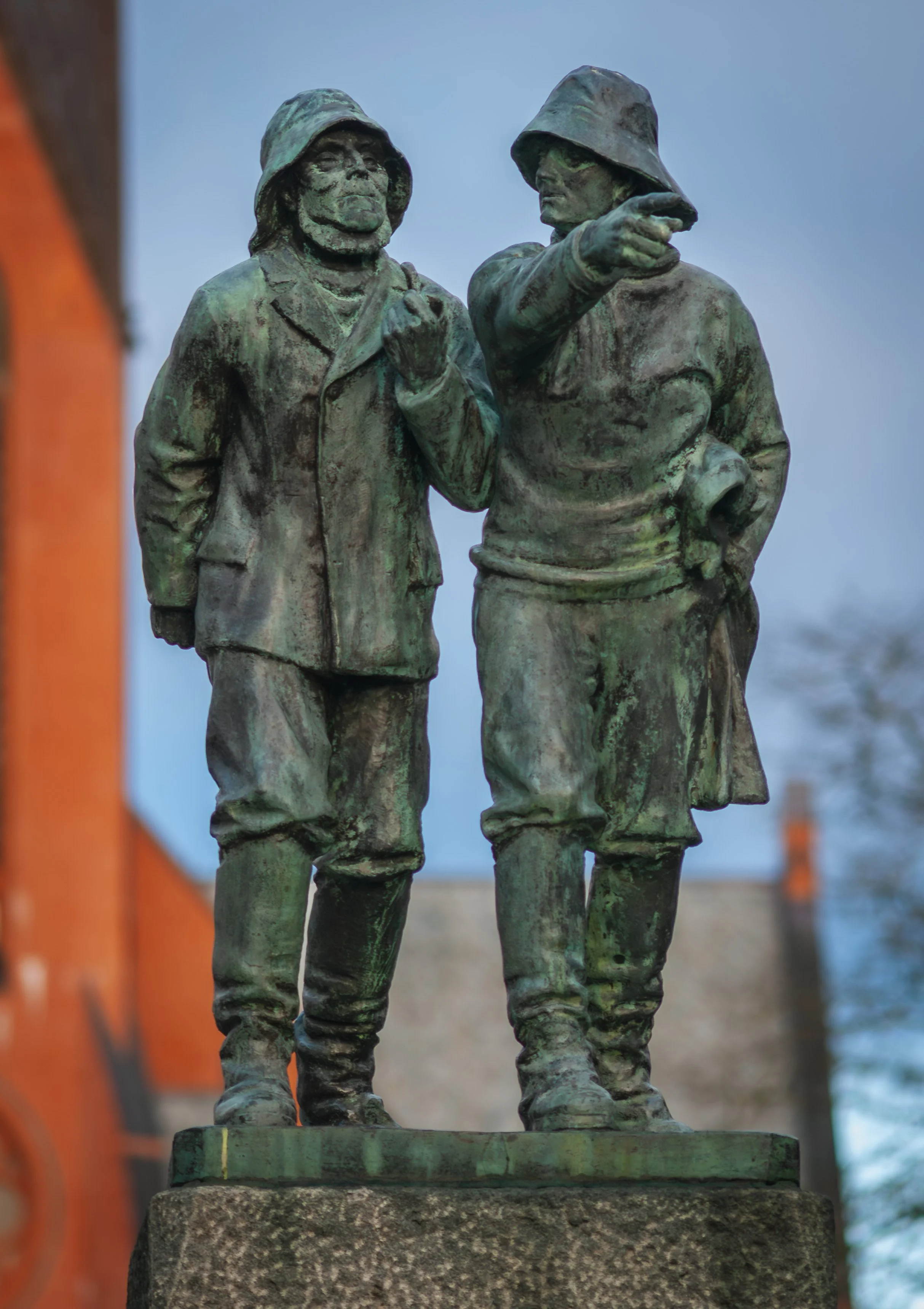 Bronze statue of two soldiers in uniforms and helmets, standing and talking with one soldier pointing and the other holding a book or paper. The statue is mounted on a stone pedestal.