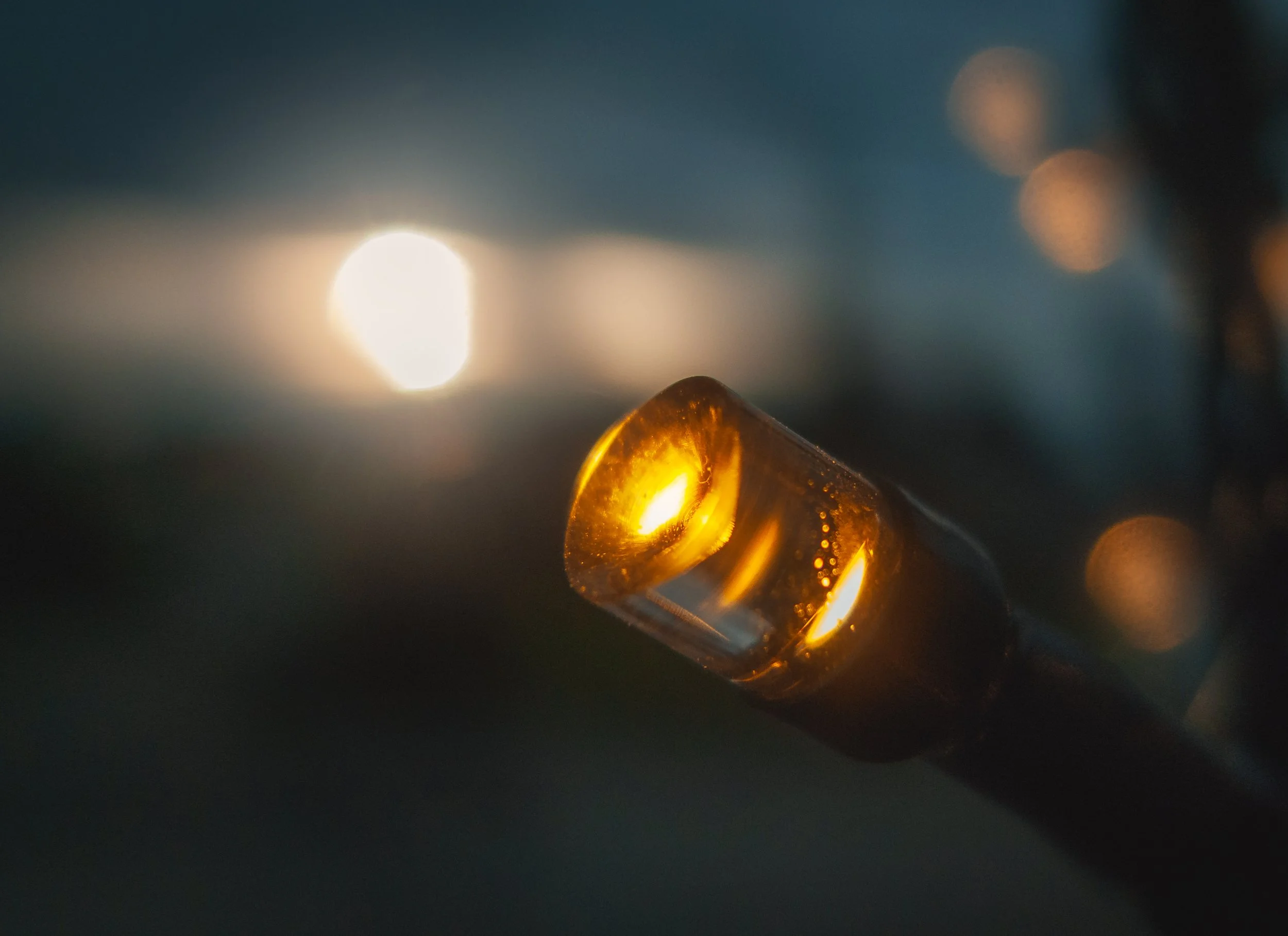 Close-up of a thermistor with a glowing orange tip, illuminated in a dark environment, with the sun in the background.