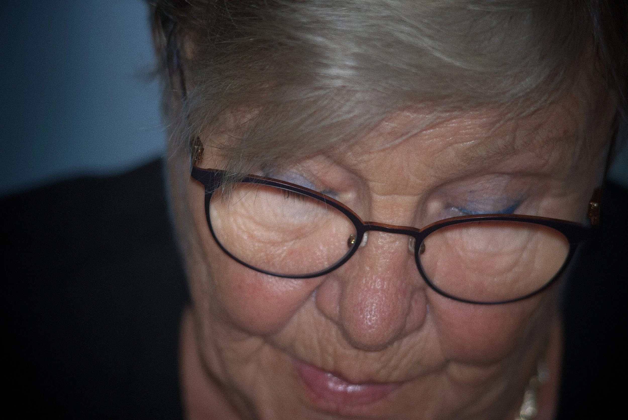 Close-up of an elderly woman with gray hair and glasses, smiling and with eyes closed.